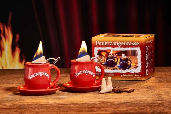 Zu sehen ist Feuerzangen 2er Set in rot. Beide Tassen sind mit der Feuerzangentassenbowle befüllt und mit einem brennenden Zuckerhut bestück
